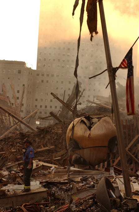 A photo of ruins at 9/11's ground zero with an American flag on a pole, an exhausted firefighter, and a burnt and damaged sphere.